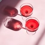 Two coupe glasses of rose wine with pink background