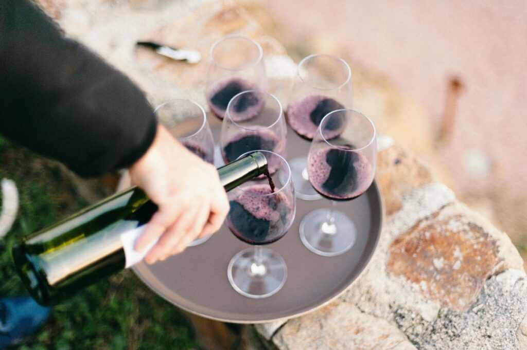 Pouring a bottle of red wine into glasses on a tray