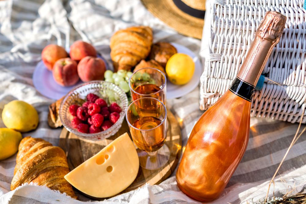 A picnic spread of apples, cheese, pastries and a bottle of sparkling wine on a blanket