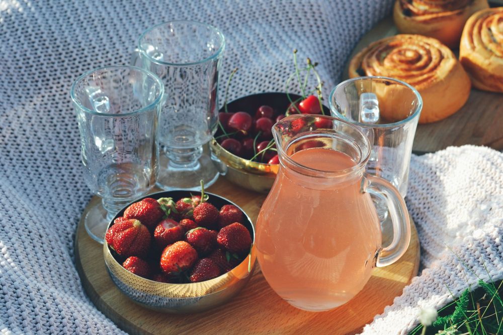 A jug of fruit drink with fresh strawberries set out on a picnic blanket