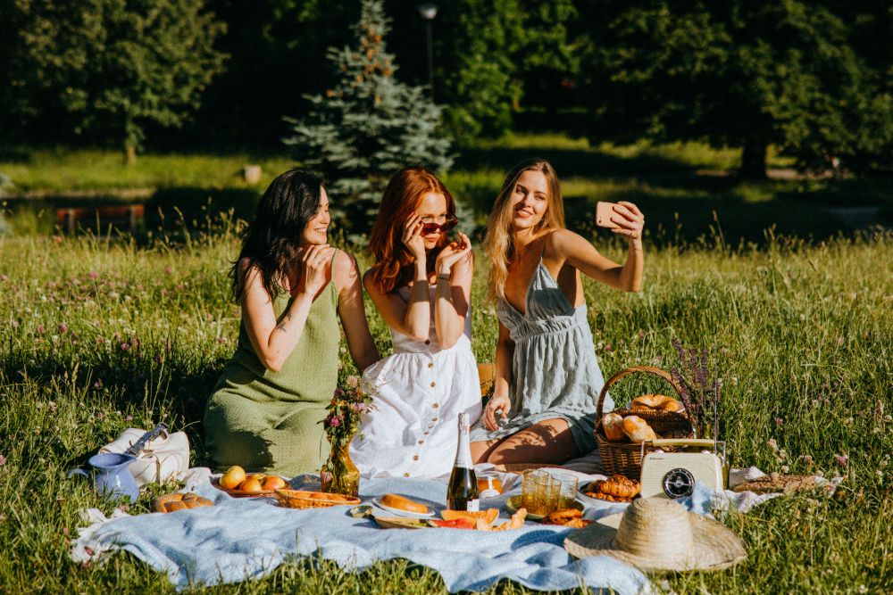 Three friends raising glasses of sparkling wine at a countryside picnic