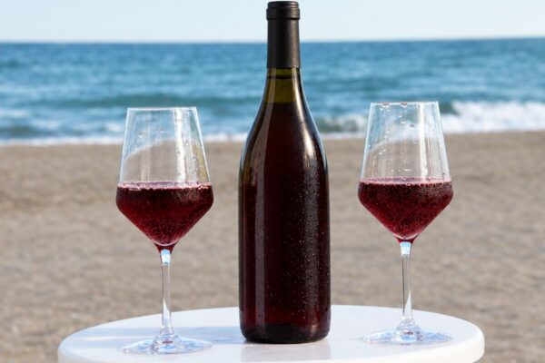 Sparkling red wine bottle with two glasses on the beach